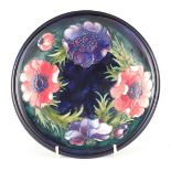 A LATE WALTER MOORCROFT SHALLOW DISH tube lined and decorated in the Anemone pattern on a dark