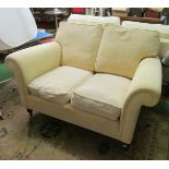 A small two seater settee upholstered in cream 62” wide