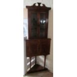 A walnut corner cabinet with two stained glass doors above two cupboard doors on tapered supports