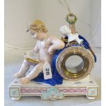 A Dresden porcelain clock case cherub reading a book with easel, column and instruments to top on