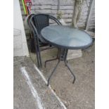 A circular black and glass garden table and a pair of chairs