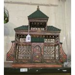 A bird cage in the form of a house with green tiled roof and painted decoration