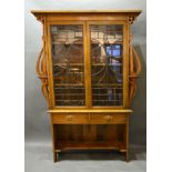 An Art Nouveau Oak Bookcase with two lead glazed doors enclosing shelves flanked by shaped pierced