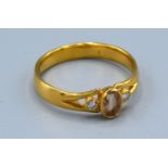 A Yellow Metal Dress Ring with a central oval stone flanked by diamonds within a pierced setting,