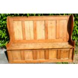 A Pine Settle with a panelled back above shaped ends with a hinged plank seat, 177 cms wide, 51