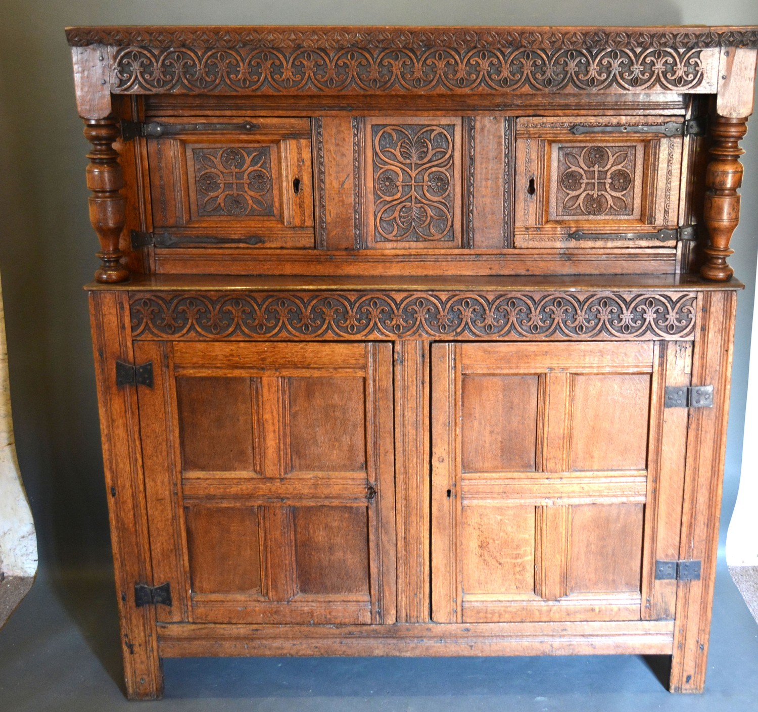 A George III Oak Court Cupboard with a carved frieze above a central carving flanked by doors, the