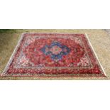 A North West Persian woollen carpet with a central medallion within an all over design upon a red,