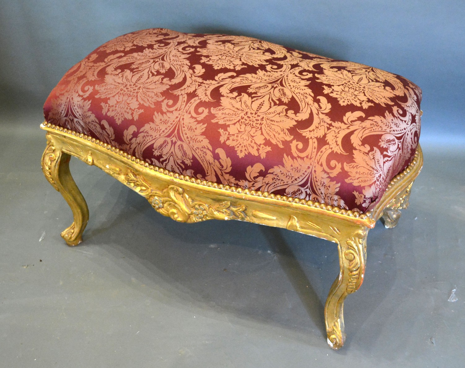 A French Style Large Gilded Stool, the burgundy upholstered top above a carved frieze raised upon