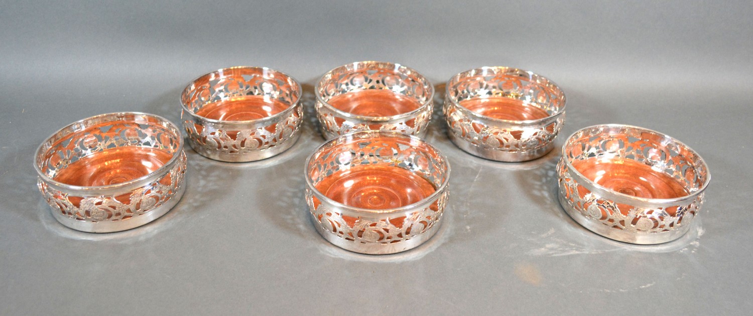 A set of six silver plated bottle coasters of pierced scroll form, with turned wooden bases, 12cms