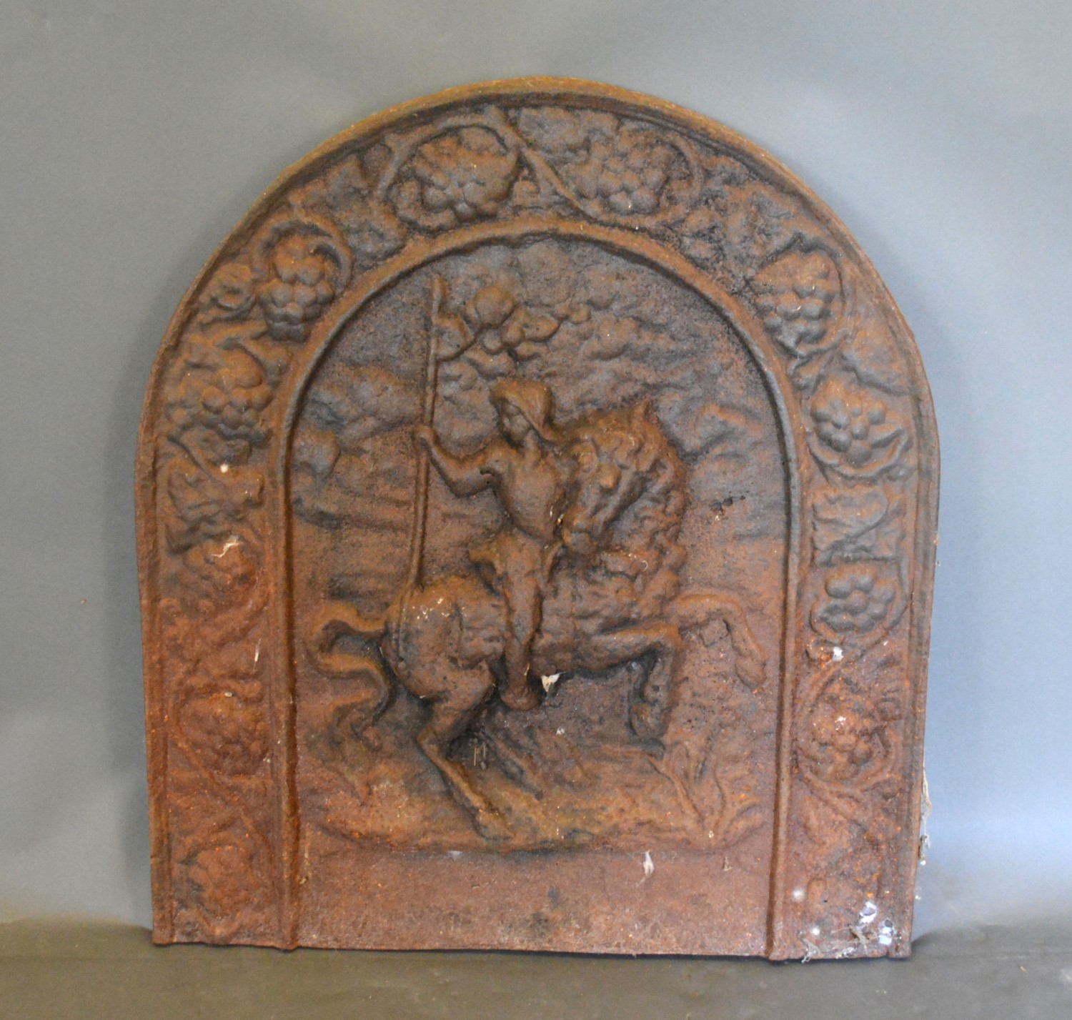 An early cast iron fire back of arched form, decorated in relief with a figure on horse back,