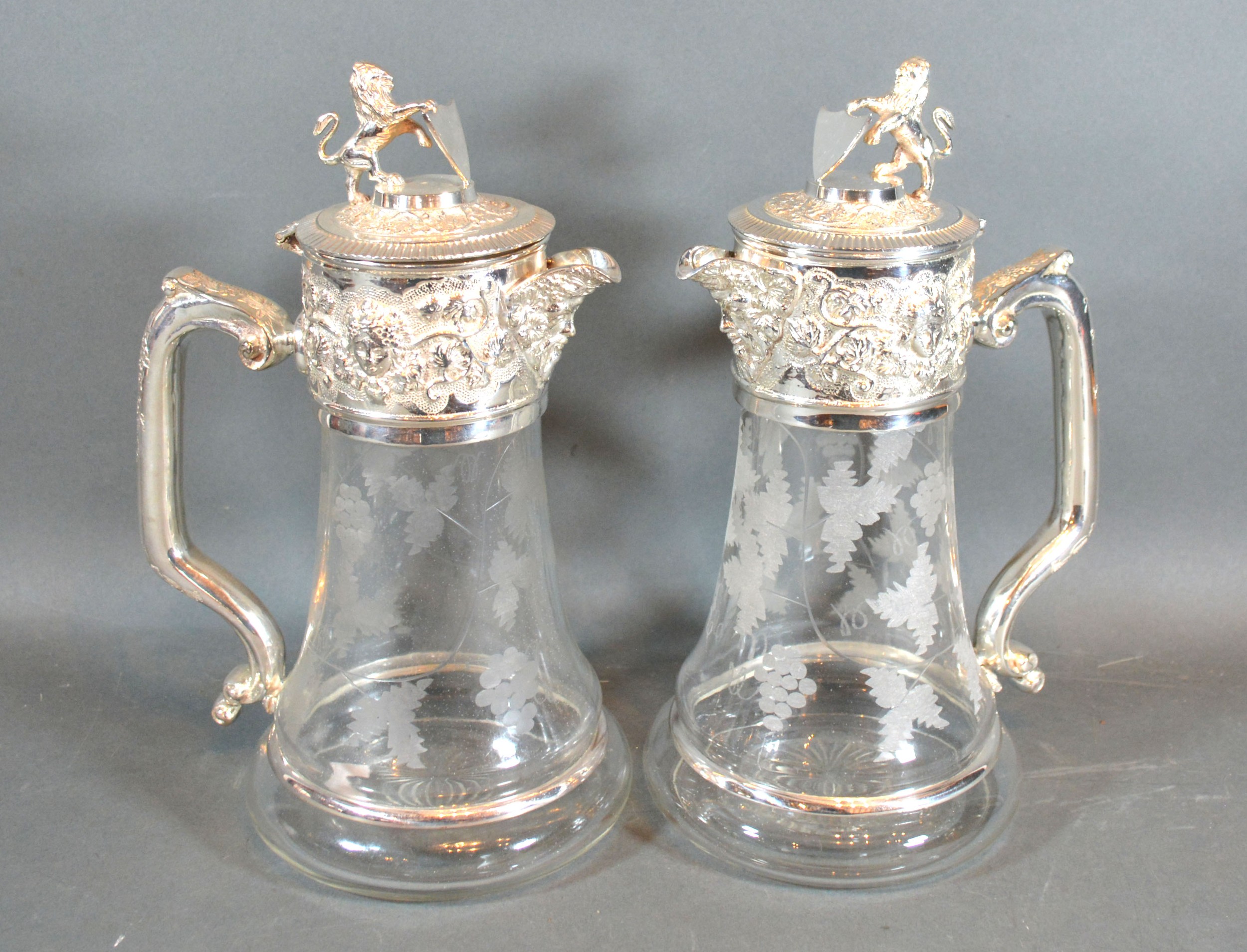 A Pair of Silver Plated and Engraved Glass Claret Jugs each with lion and shield mounts with