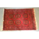 A Bokhara Woollen Rug with two rows of guls upon a red blue and cream ground within multiple