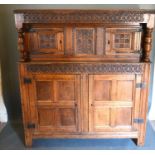 A George III Oak Court Cupboard with a carved frieze above a central carving flanked by doors, the
