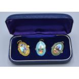 A Set of Three Enamel Pendant Lockets hand painted with oval scenes within fitted case