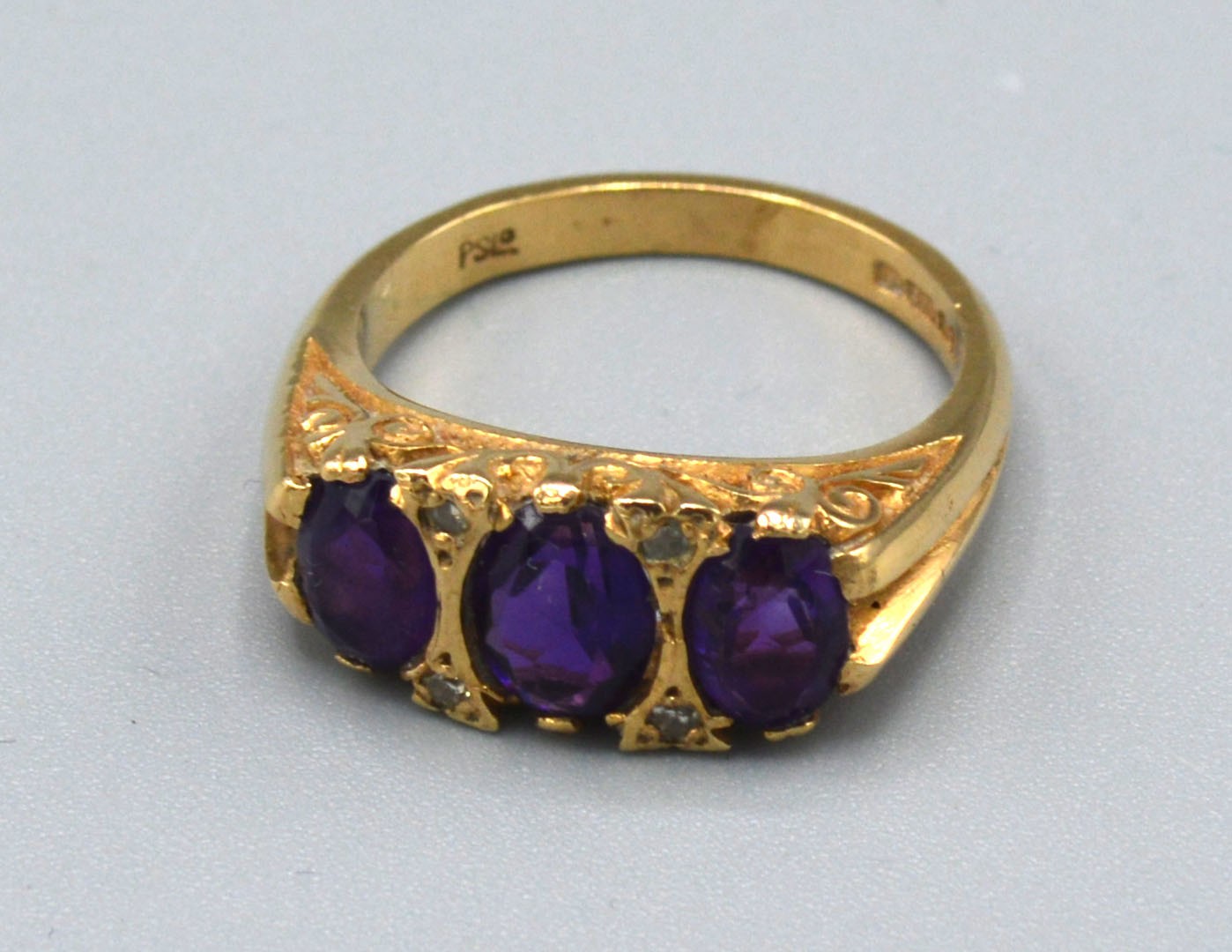 A 9ct. Gold Dress Ring set three amethysts interspaced with diamonds within a pierced scroll