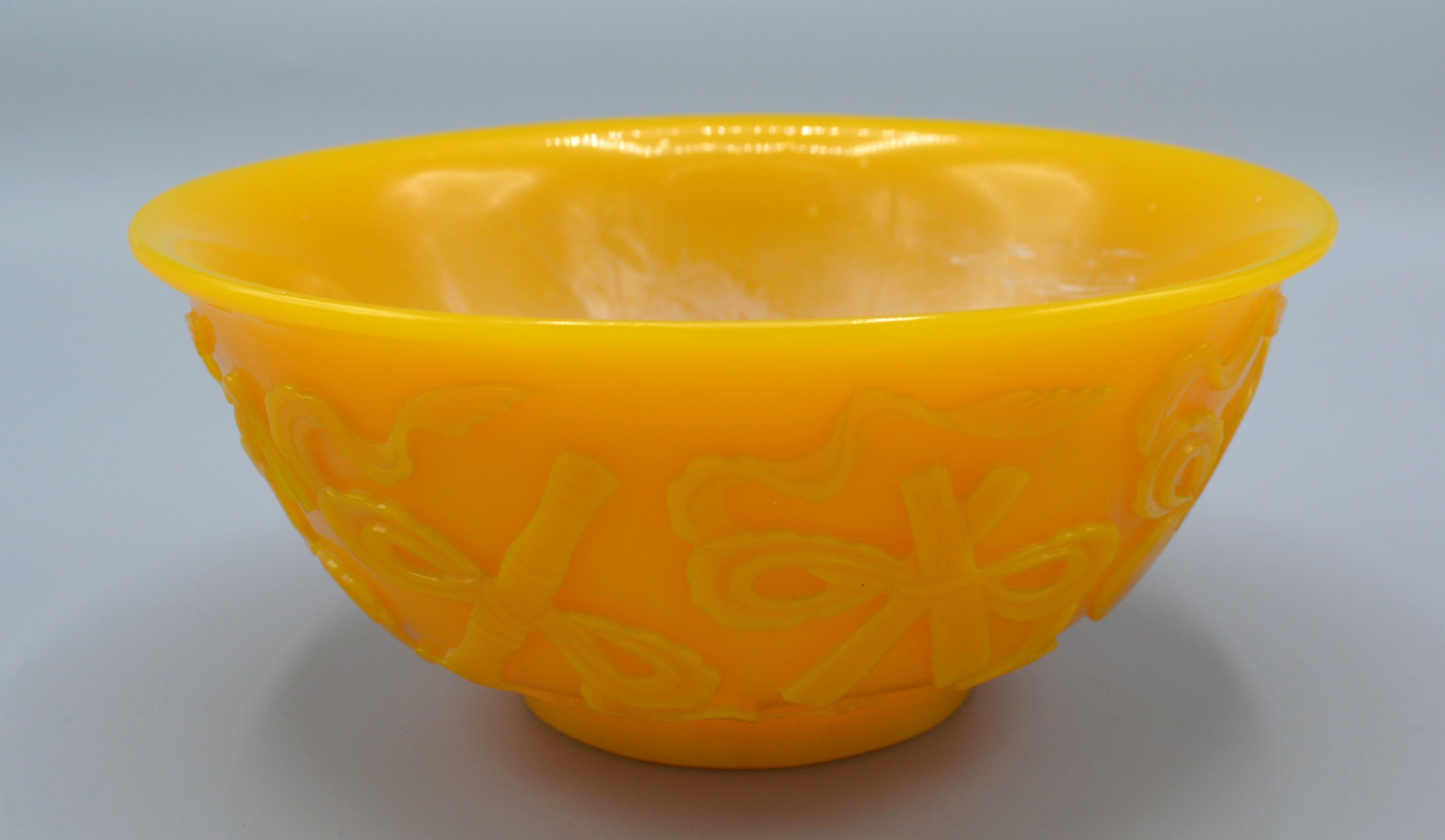 A Chinese Yellow Glass Bowl carved in relief with implements and scrolls, 15.5 cms diameter