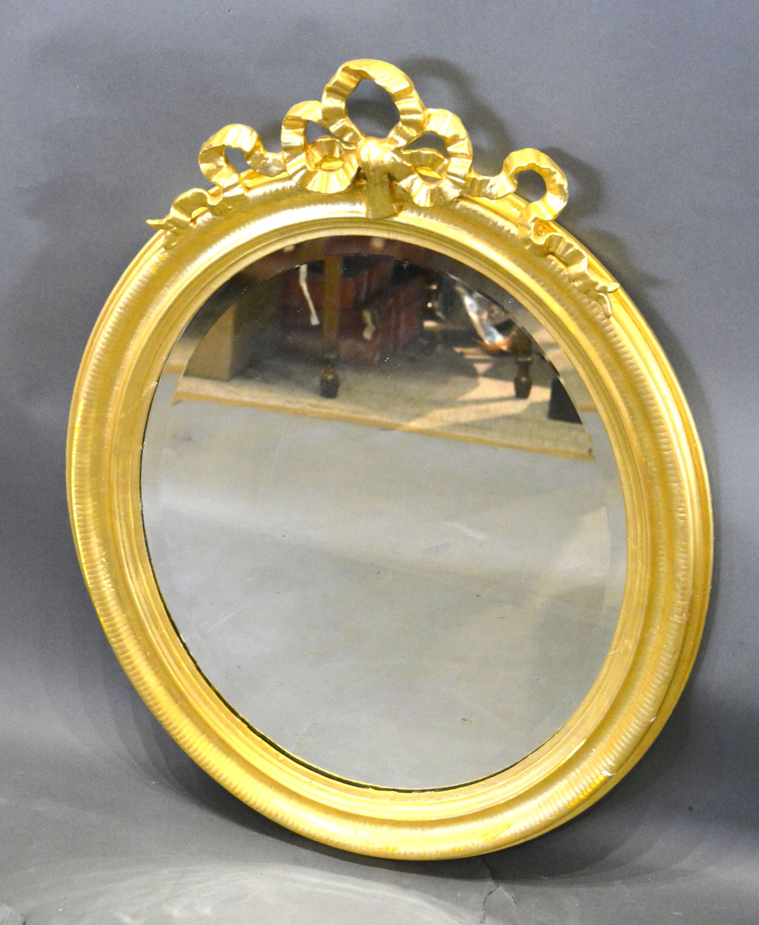 A Late 19th Early 20th Century French Oval Gilded Wall Mirror with bow cresting and bevelled glass