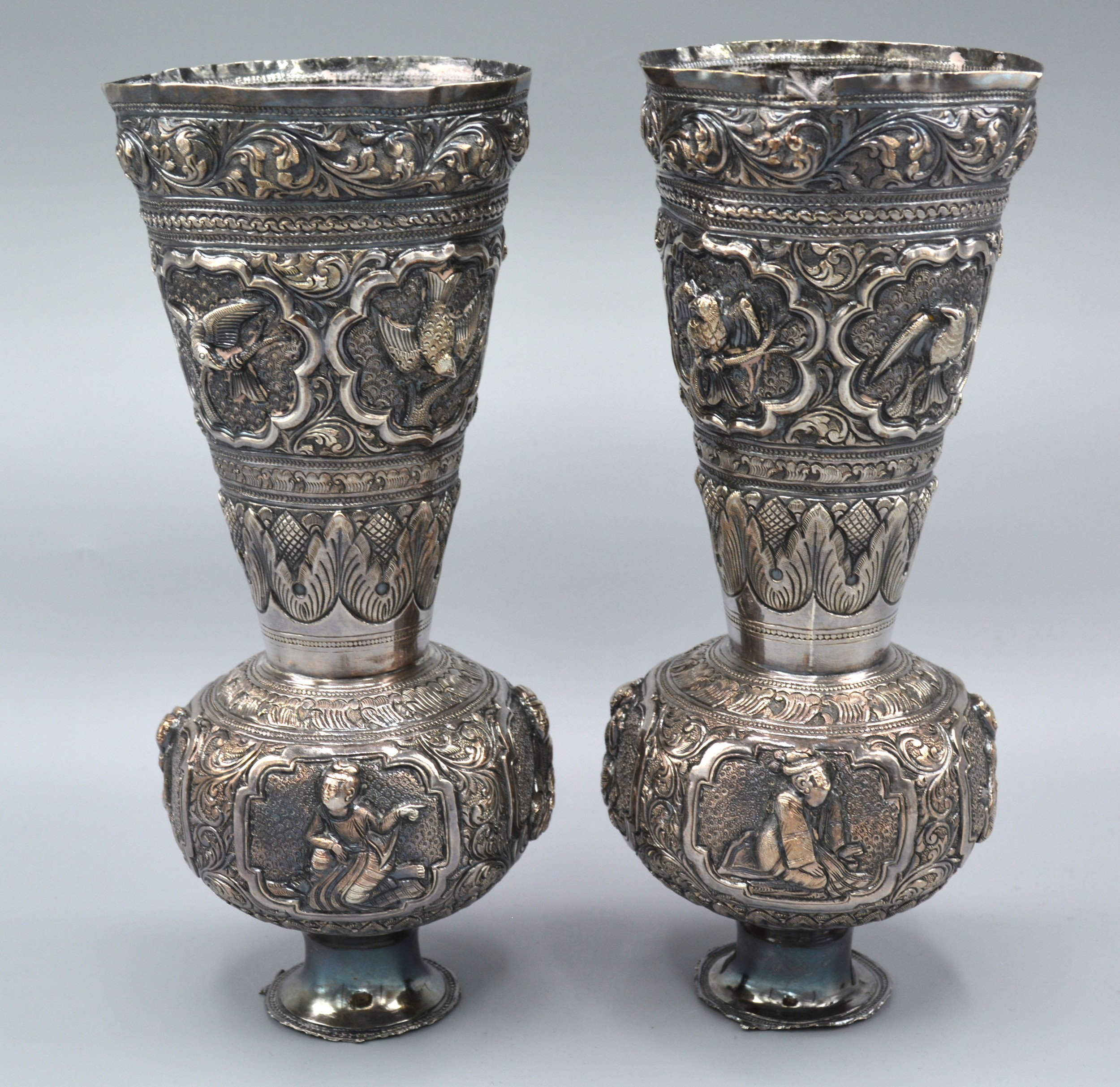 A Pair of Indian White Metal Spill Vases decorated in relief with figures and birds 19 cms tall