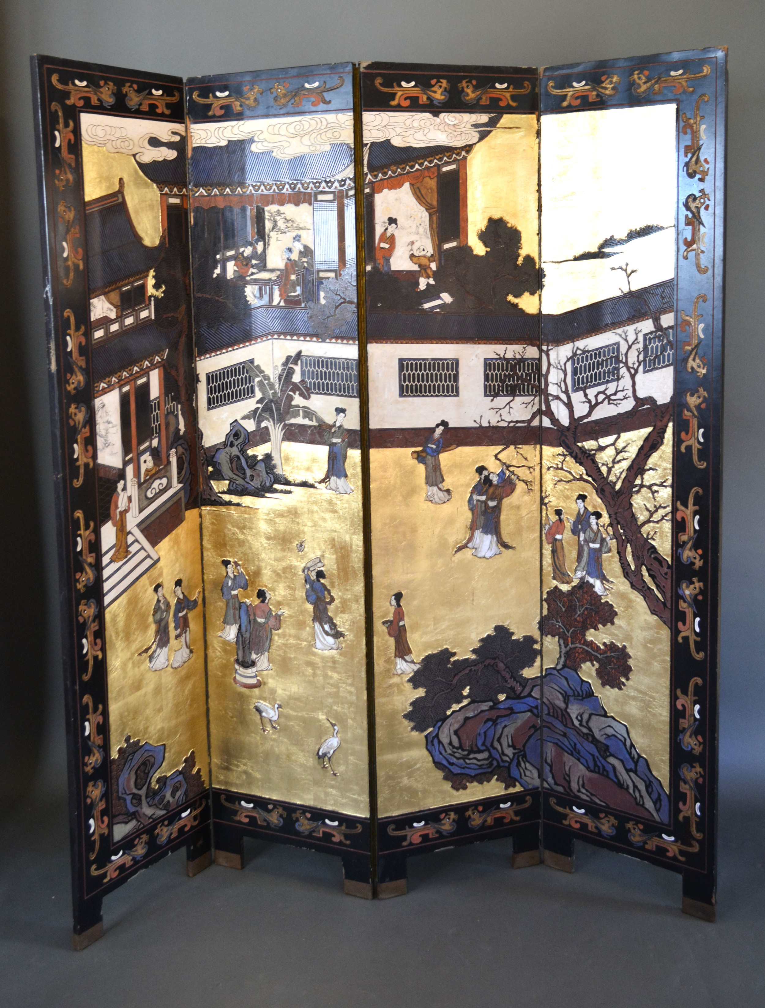 A Chinese Lacquered Four Fold Screen depicting figures within a landscape amongst buildings, the