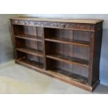 A Victorian Carved Oak Dwarf Long Bookcase with a carved frieze above an arrangement of shelves upon