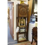 An Arts and Crafts oak long case clock, the face with brass numerals and hands, above open shelves.