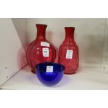 Two cranberry glass bottle vases and a blue glass bowl.