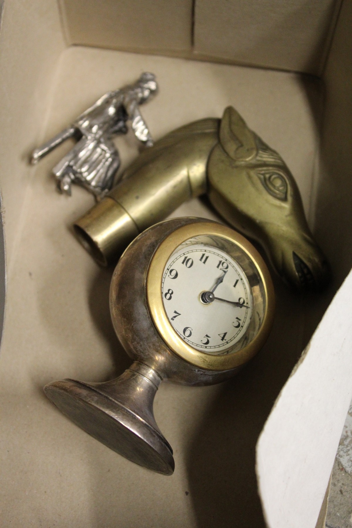 A small clock, a horse's head walking stick handle and a chrome figure.