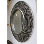 A circular wall mirror with decorative silver coloured frame.