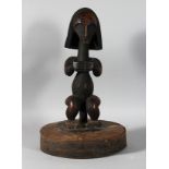 A CARVED TRIBAL AFRICAN FIGURE on an oval base. 19ins high.