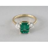A SUPERB 18CT GOLD THREE-STONE EMERALD AND DIAMOND RING.