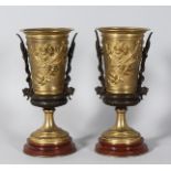 A PAIR OF CLASSIC BRONZE AND GILT BRONZE URNS on circular bases. 9.5ins high.