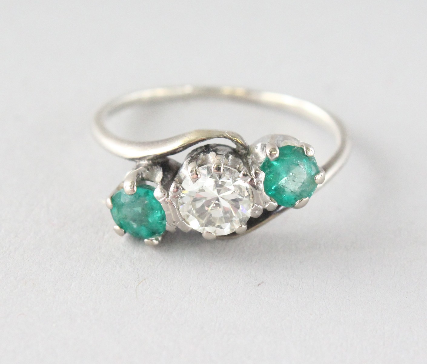 AN 18CT GOLD THREE-STONE DIAMOND AND EMERALD RING.