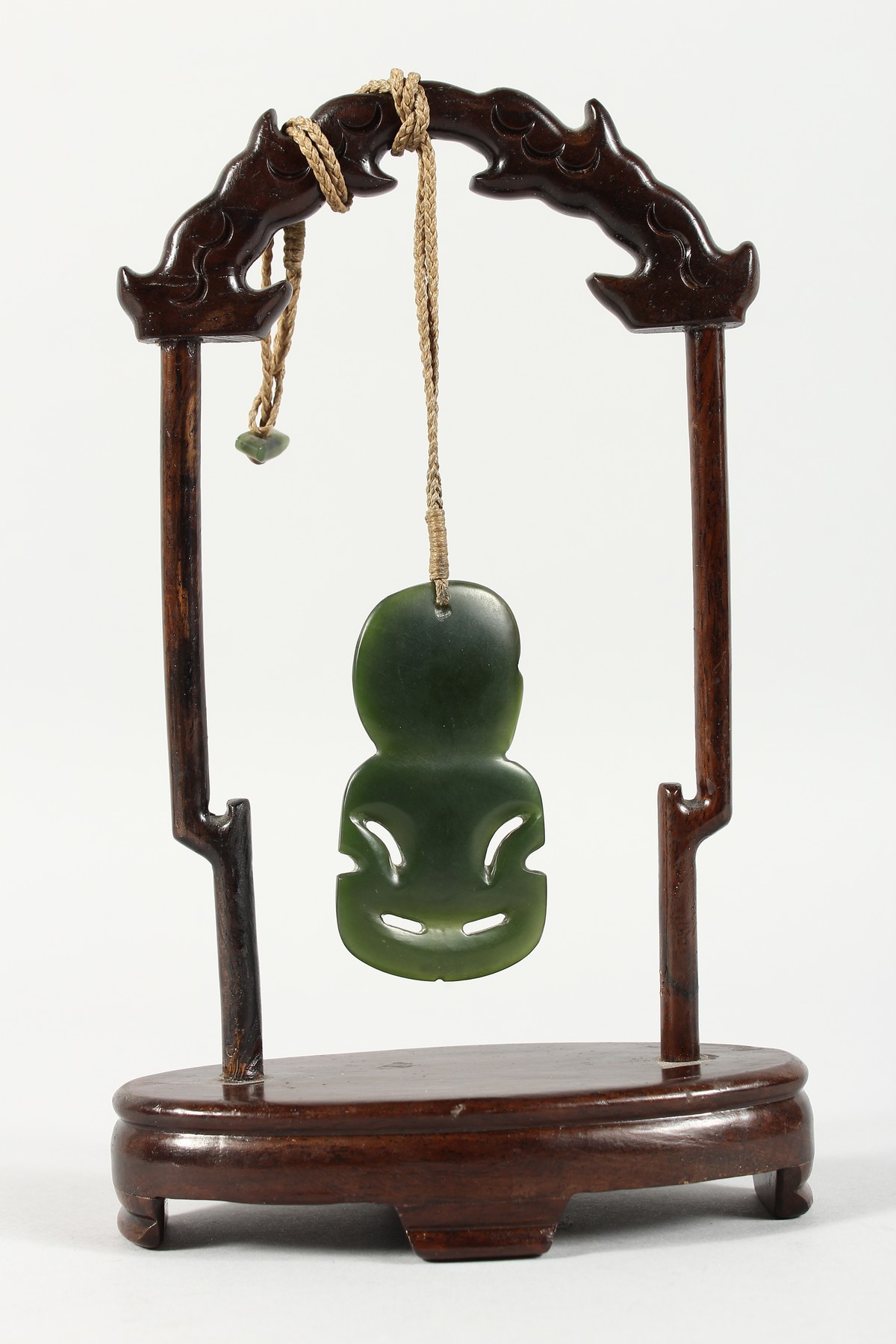 A NEW ZEALAND CARVED JADE TIKKI, suspended from a hardwood frame. Tikki: 2.75ins high. - Image 4 of 5