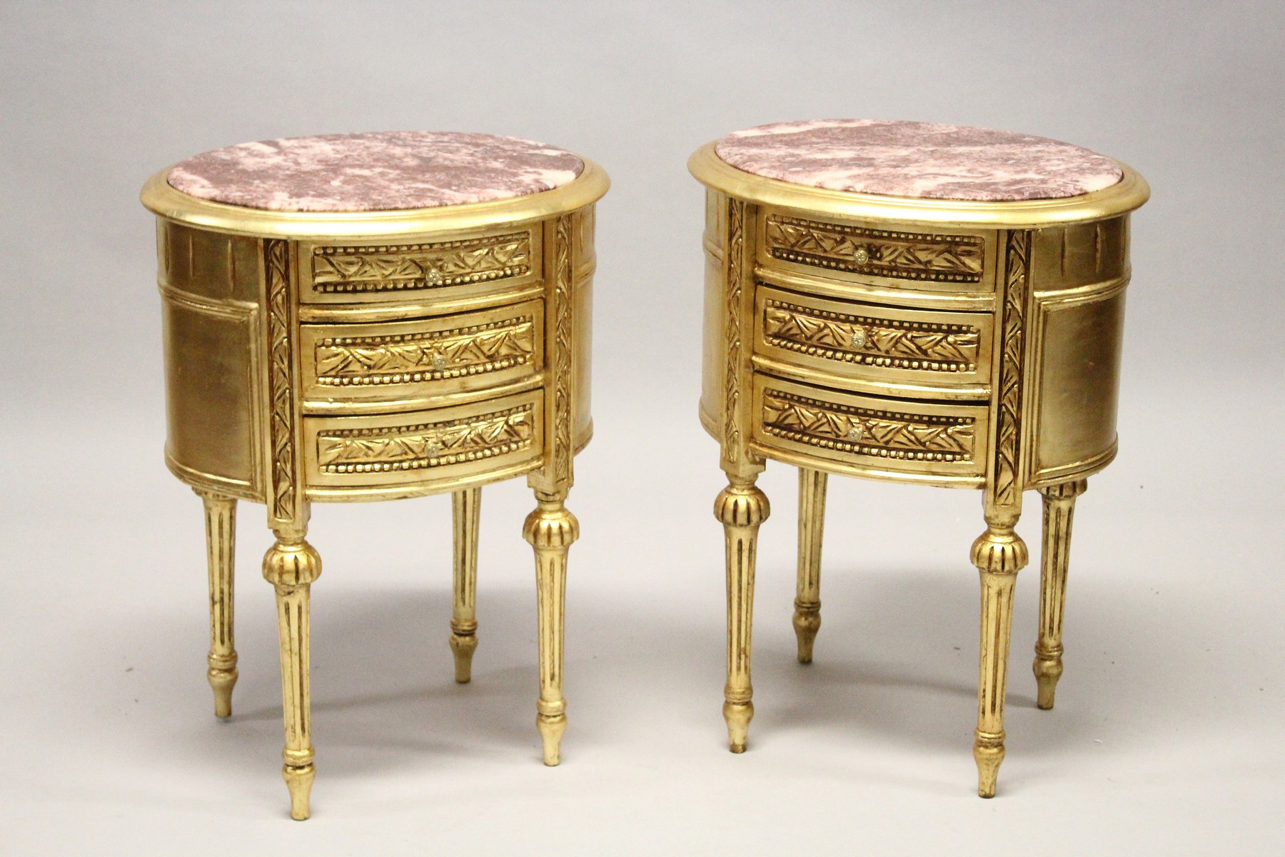 A GOOD PAIR OF THREE DRAWER GILT BEDSIDE TABLES with oval marble tops. 27ins high.