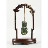 A NEW ZEALAND CARVED JADE TIKKI, suspended from a hardwood frame. Tikki: 2.75ins high.