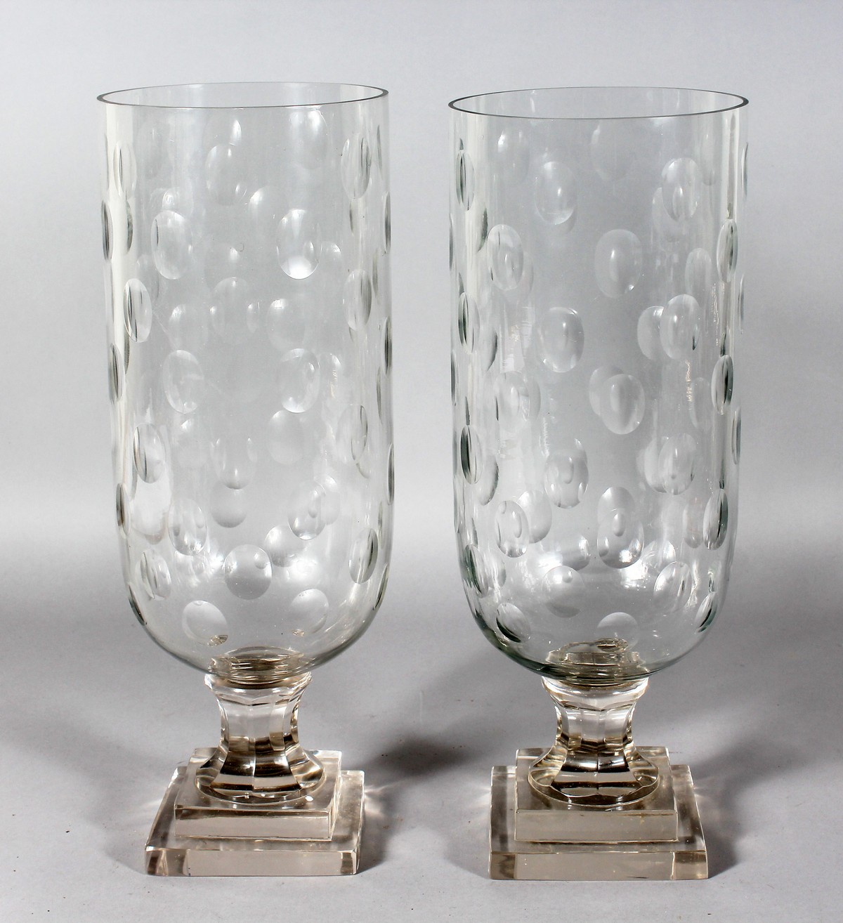 A PAIR OF OVAL CUT CIRCULAR GLASS STORM LAMPS on square stepped bases. 16ins high.