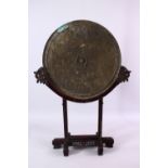 A LARGE CHINESE CIRCULAR CAST BRONZE 'MIRROR' on a hardwood stand (stand AF), disc 46cm diameter.