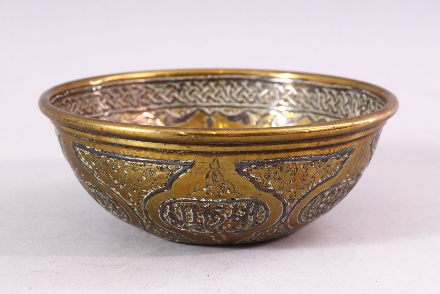 A SMALL ISLAMIC CIRCULAR BRASS BOWL with silver inlaid and engraved decoration, 13cm diameter.