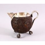 A FINELY CARVED THAI COCONUT JUG WITH SILVER MOUNTS, on three ball feet, 10cm high .