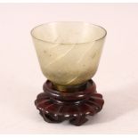 A GOOD JADE CUP on a wooden stand. 2.5ins diameter.