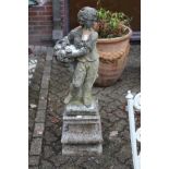 A composite garden figure of a young boy holding a basket of flowers on a pedestal base.