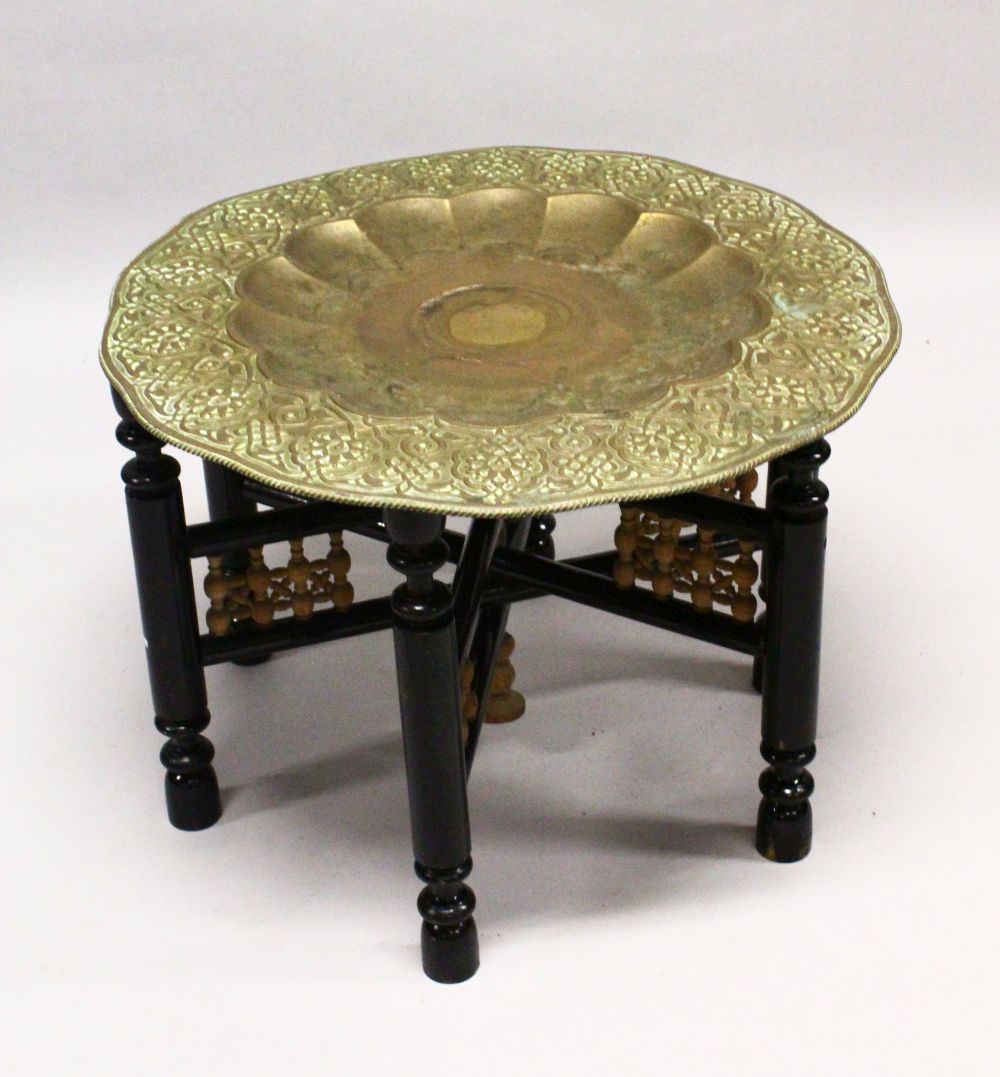 A GOOD LARGE ISLAMIC BRASS TRAY TABLE AND FOLDING STAND, with embossed decoration, 76cm diameter.