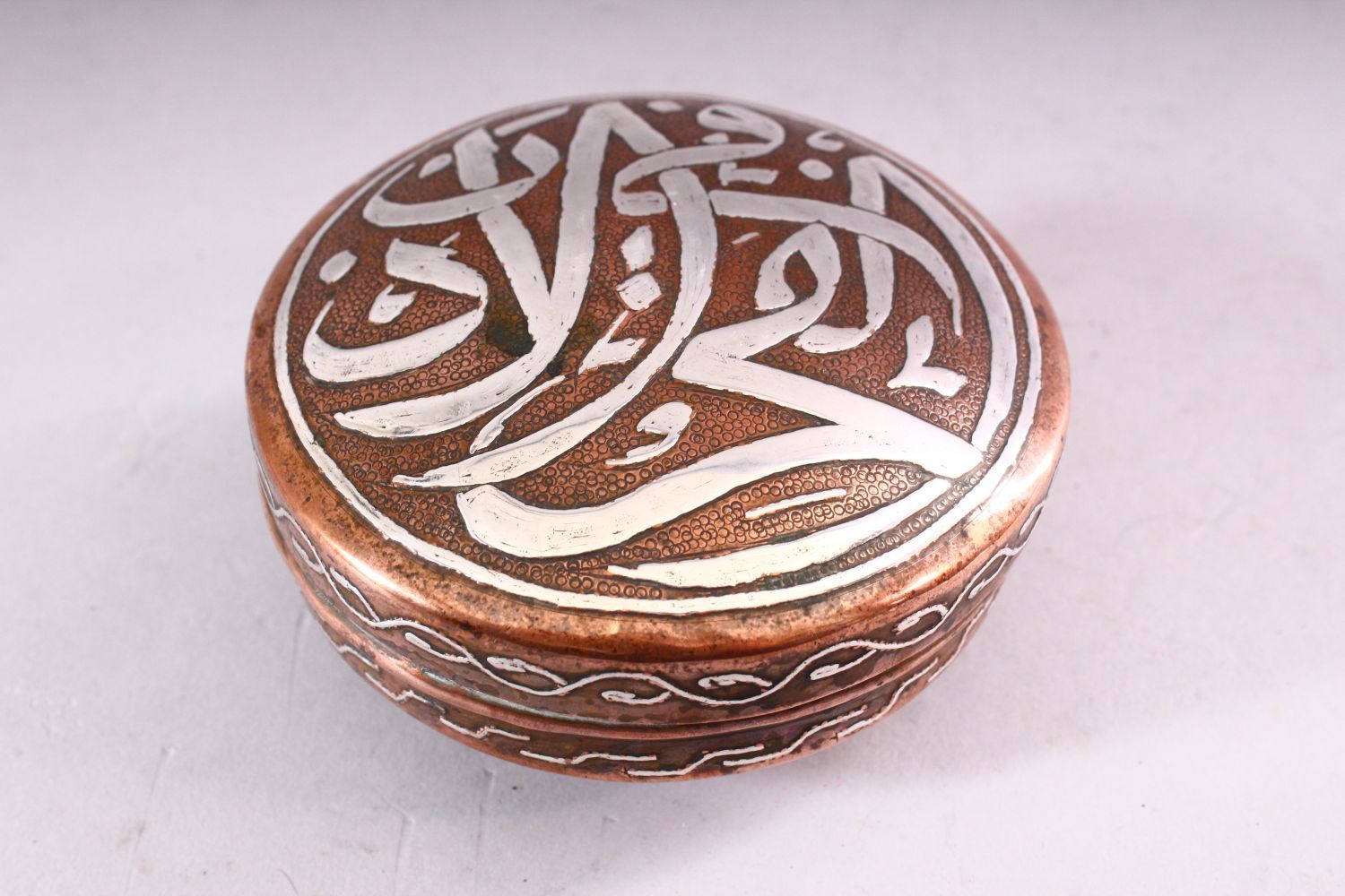 AN ISLAMIC CIRCULAR COPPER BOX AND COVER, the cover with silver inlaid calligraphy, 10cm diameter. - Image 3 of 5