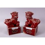 A PAIR OF CHINESE COPPER RED PORCELAIN TEMPLE LIONS, each posed upon a fixed base with their paw