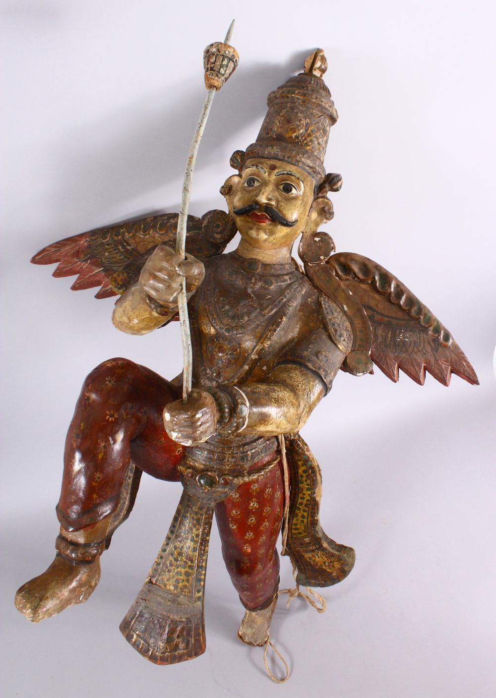 A 19TH CENTURY INDIAN / BURMESE CARVED WOOD FIGURE OF A WINGED GOD, stood holding an implement, with