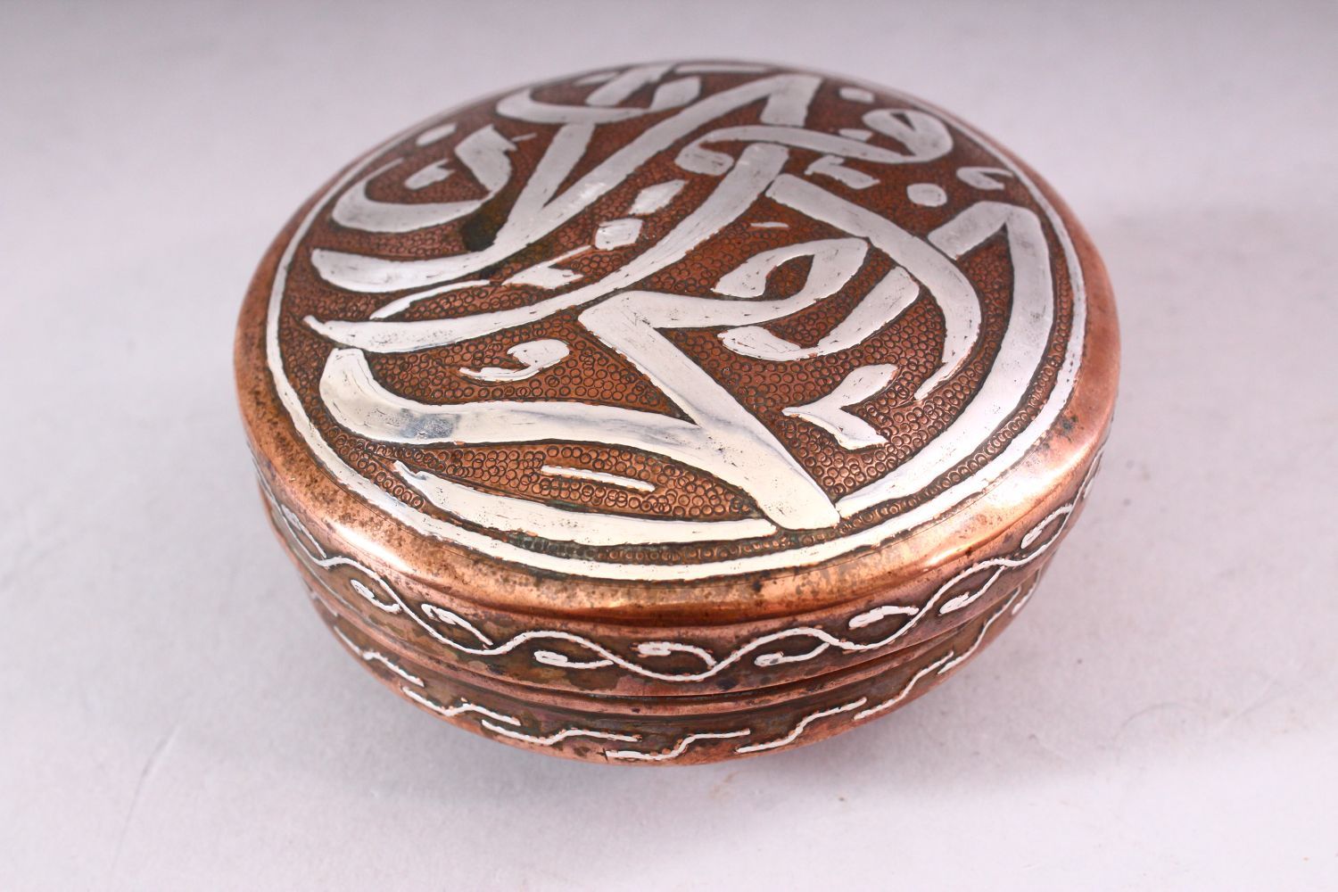 AN ISLAMIC CIRCULAR COPPER BOX AND COVER, the cover with silver inlaid calligraphy, 10cm diameter. - Image 2 of 5