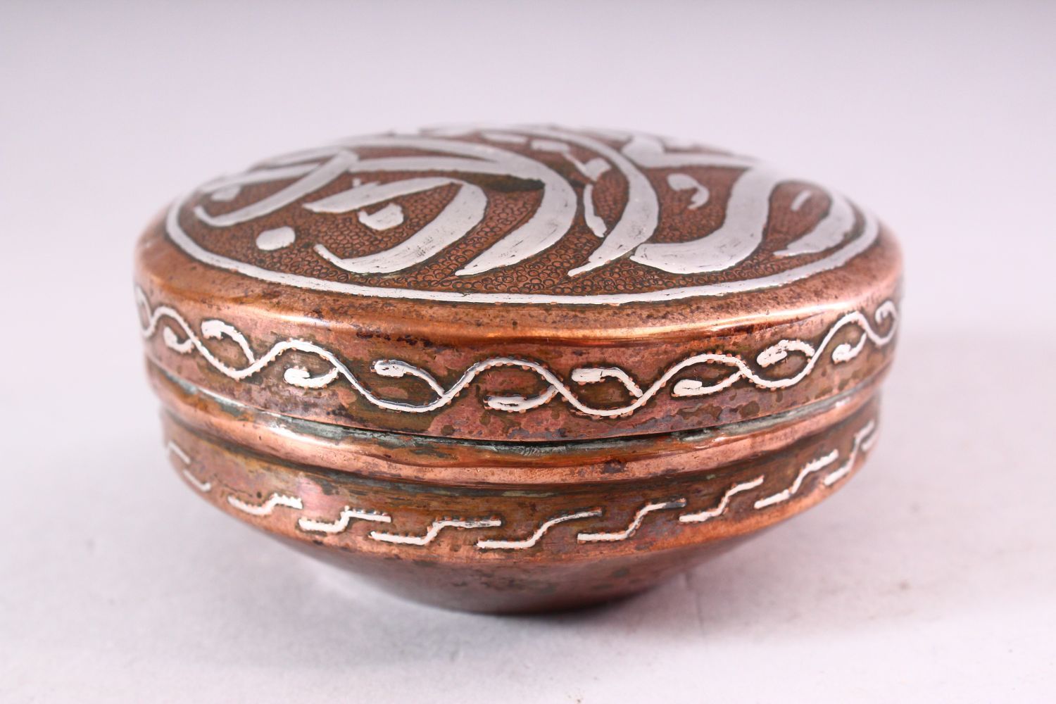 AN ISLAMIC CIRCULAR COPPER BOX AND COVER, the cover with silver inlaid calligraphy, 10cm diameter. - Image 4 of 5