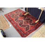A Persian rug, red ground with three large diamond shaped central motifs.