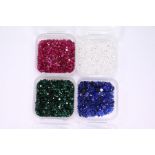 Four small boxes containing small gemstones, comprising rubies, sapphires, emeralds and spinels.