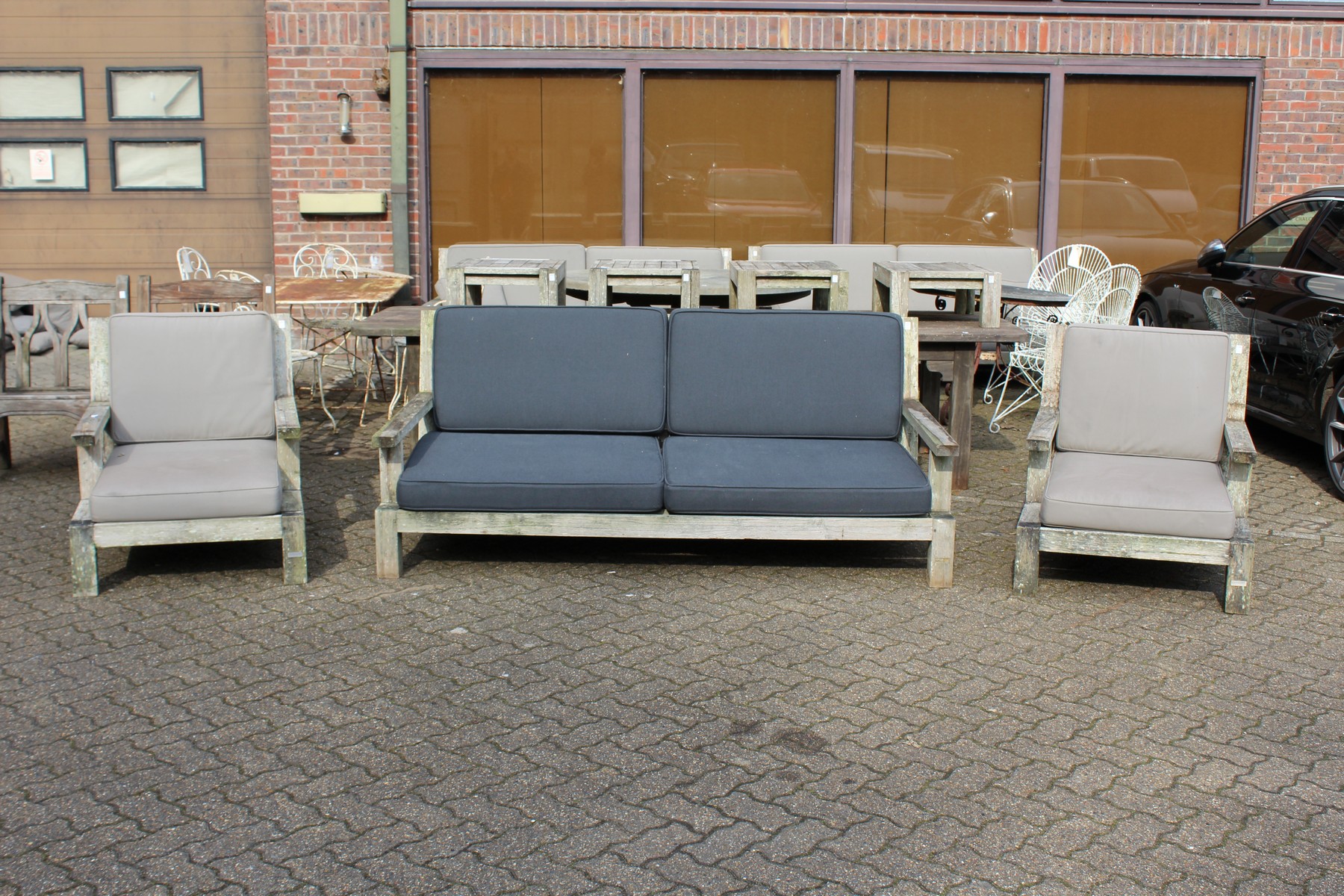 A large teak garden settee with a pair of lounger style armchairs with loose cushions.